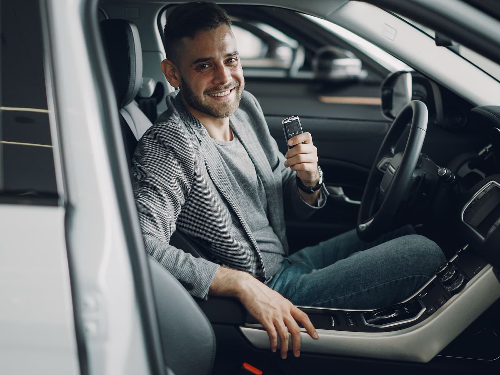 Dealer sonriente en el asiento de su vehículo, con la llave en la mano.